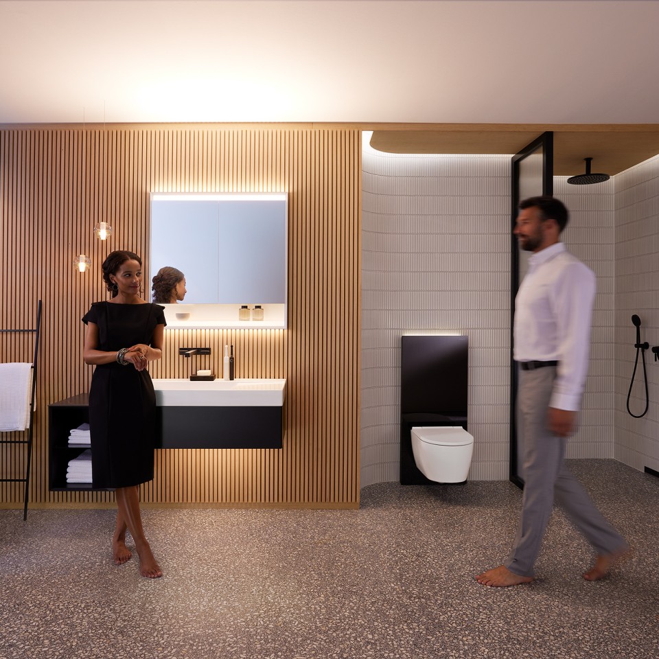 Egy férfi és egy nő egy Geberit ONE fürdőszobabútorokkal és kerámiákkal berendezett, harmonikusan megvilágított fürdőszobában (© Geberit)