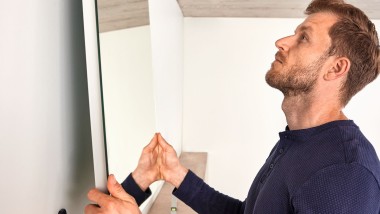 Egy férfi fürdőszoba-felújítás közben felekaszt egy Geberit Option tükröt