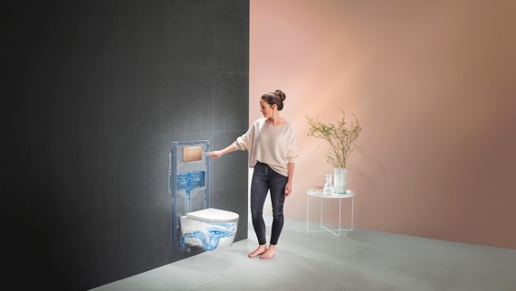 Egy nő elindítja az öblítést a Geberit WC-rendszerben (© Geberit)