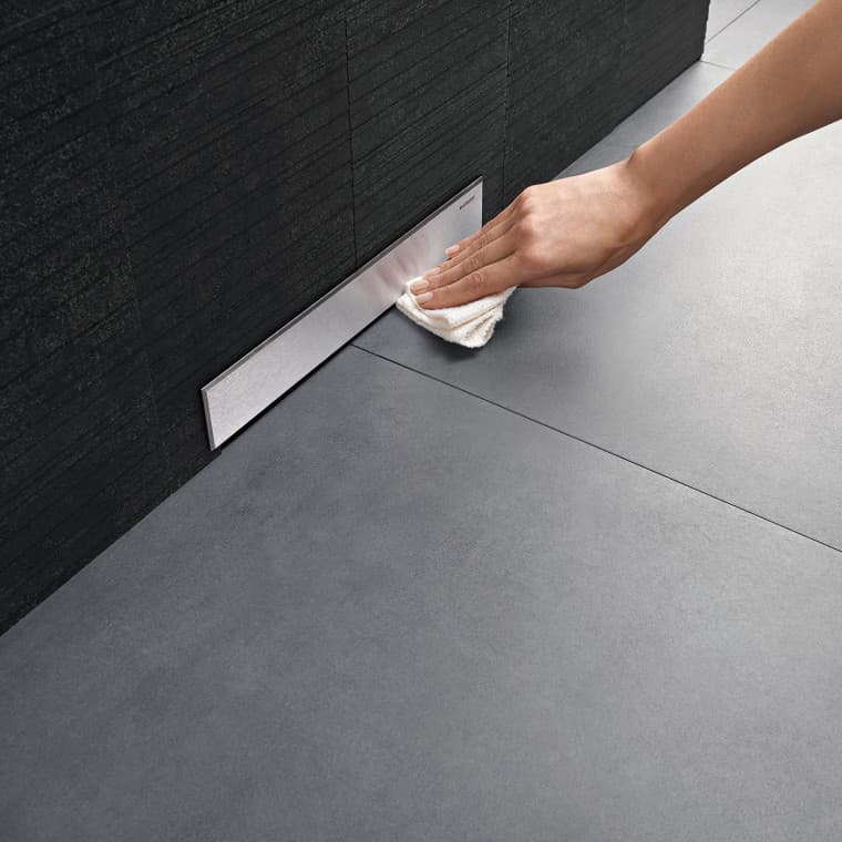 Egy kéz tisztítja a Geberit falba rejtett lefolyó szelepfedelét Egy kéz tisztítja a Geberit falba rejtett lefolyó szelepfedelét